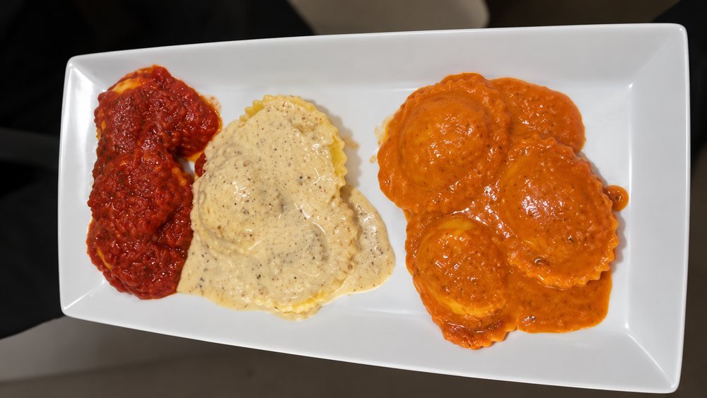 Ravioli served with three sauces on a white plate.
